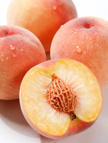 אפרסקים שלמים ופרוסים על שולחן עץ, לצד כוס מיץ אפרסק